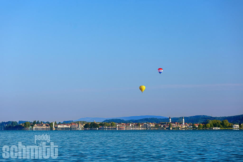 Ballone über Lindau am Bodensee | Heißluftballone schweben über Lindau am Bodensee und setzen farbenfrohe Akzente am Himmel. Über der Insel und dem weiten See entsteht ein leichtes, lebendiges Motiv voller Weite und sommerlicher Atmosphäre. - Realisiert mit Pictrs.com