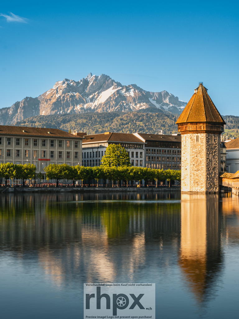 Kapellbrücke und Pilatus im Morgenlicht, Luzern | Die Kapellbrücke mit dem Wasserturm spiegelt sich ruhig in der Reuss, während im Hintergrund der Pilatus im klaren Morgenlicht erscheint. Klassische Luzerner Ansicht mit sauberer Linienführung, warmem Licht und ruhiger Wasseroberfläche – ein zeitloses Postkartenmotiv mit alpinem Bezug. - Realisiert mit Pictrs.com