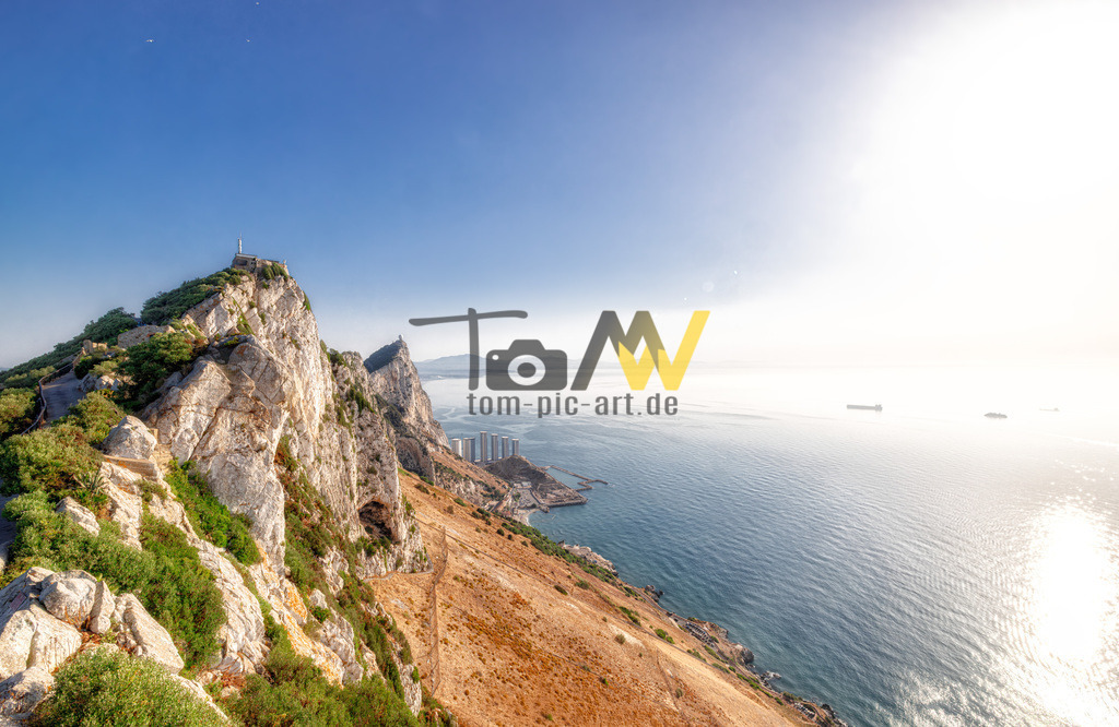 Blick über den Felsen von Gibraltar auf den blauen Ozean | Das Bild zeigt den Felsen von Gibraltar (Rock of Gibraltar), ein britisches Überseegebiet an der Südspitze Europas. Der Felsen ist ein monolithischer Kalksteinfelsen, der den größten Teil der Halbinsel einnimmt und an seiner höchsten Stelle 426 Meter misst. Er markiert die strategisch wichtige Verbindung zwischen dem Atlantik und dem Mittelmeer. Ein Großteil des oberen Felsens ist ein Naturschutzgebiet, bekannt für seine Population der Berberaffen, die die einzigen wilden Affen in Europa sind.  - Realisiert mit Pictrs.com