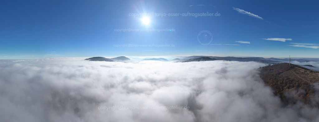 Erstaunliches Wolkenpanorama über Hoppecke | Panorama Luftbild zeigt tief schwebende Wolken über dem <a href="https://www.google.com/search?q=Gro%C3%9Fer%20Buttenberg" target="_blank">Großer Buttenberg</a> bei Brilon <a href="https://www.google.com/search?q=Hoppecke" target="_blank">Hoppecke</a> von oben. Darüber ist blauer Himmel und Sonnenschein. Der Funkturm und verschiedene Berggipfel ragen durch die Wolken. Eine kleine Ortschaft ist neben dem Funkturm zu erkennen. Foto aus dem Hochsauerland.