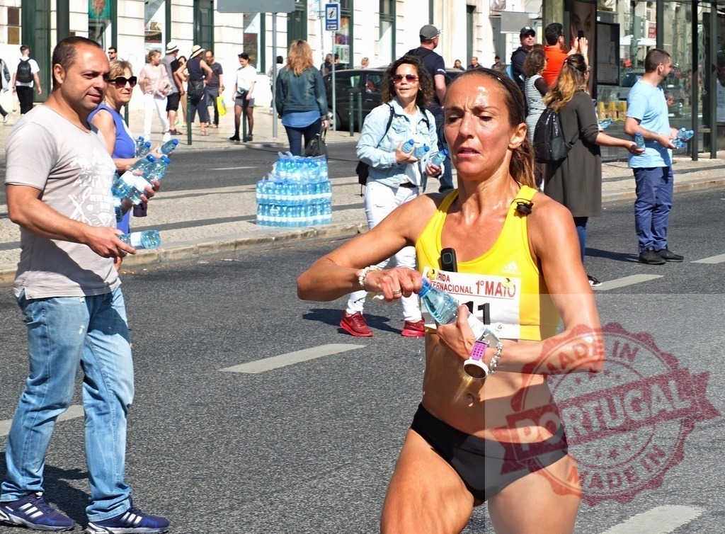 Female runner hydrating during a marathon race on city street | Sweaty woman athlete opening a water bottle while running and looking tired - Realisiert mit Pictrs.com