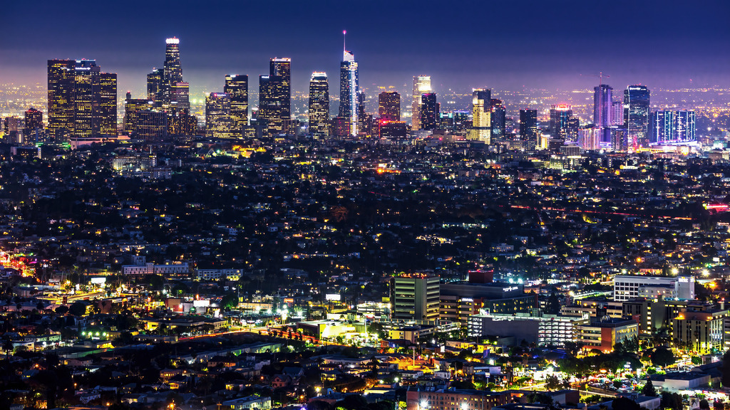 Wandbild - Los Angeles Stadtlichter der Nacht | Dieses beeindruckende Bild zeigt eine nächtliche Skyline von Los Angeles, die in einem funkelnden Lichtermeer erstrahlt. Die hohen Wolkenkratzer und Gebäude leuchten in verschiedenen Farben und dominieren den nächtlichen Himmel. Die Stadt erstreckt sich weit, und die vielen Lichter der Straßen und Häuser schaffen ein lebendiges und pulsierendes Ambiente. Der Kontrast zwischen den dunklen Silhouetten der Gebäude und den hellen Lichtern erzeugt eine dynamische und fesselnde Szene, die die Energie und das Leben der Stadt bei Nacht einfängt.