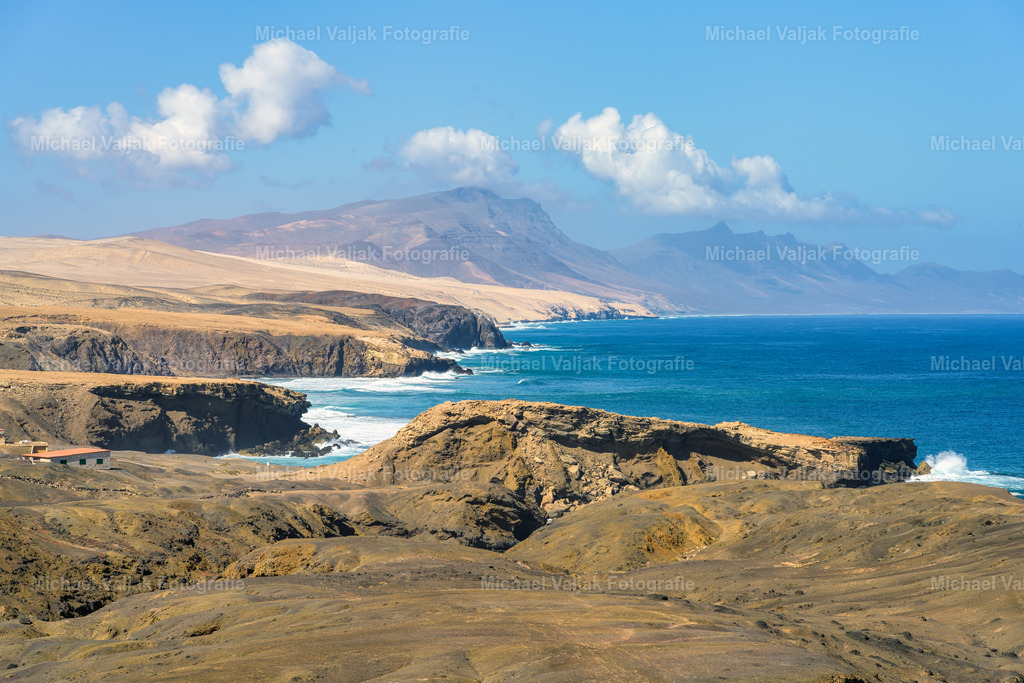 Küste bei La Pared auf Fuerteventura | Die Küste bei La Pared zeigt sich auf diesem Foto von ihrer typischen, kraftvollen Seite. Die dunklen Felsformationen fallen steil zum Atlantik ab, während die Wellen mit spürbarer Energie gegen die Klippen schlagen. Das Licht hebt die rauen Strukturen des Gesteins hervor und lässt die unterschiedlichen Farbtöne der Felsen klar hervortreten. Über dem Meer öffnet sich der Blick in die Weite, und die Brandung zeichnet helle Linien entlang der Küste. Ein Moment, der die wilde, unverfälschte Natur der Westseite Fuerteventuras eindrucksvoll festhält. - Realisiert mit Pictrs.com