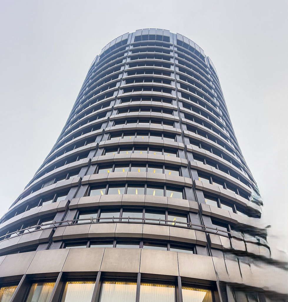 Urban Ascension | A futuristic architectural perspective of the BIZ Tower in Basel, captured from below with subtle reflections and distortion effects that transform the structure into an almost surreal urban form. - Realisiert mit Pictrs.com