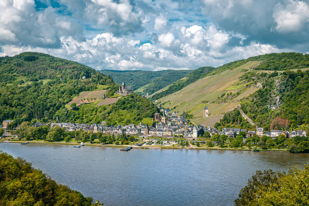 Blick auf die historische Stadt Bacharach am Rhein und Burg Stahleck | Diese Aufnahme zeigt die historische Stadt Bacharach am Rhein im UNESCO-Welterbe Oberes Mittelrheintal.Burg Stahleck: Auf der Anhöhe über der Stadt thront die Burg Stahleck, die heute als eine der bekanntesten und malerischsten Jugendherbergen Deutschlands genutzt wird.Wernerkapelle &amp; Stadtbild: Unterhalb der Burg sind die gotische Ruine der Wernerkapelle sowie die markante evangelische Pfarrkirche St. Peter zu erkennen, eingebettet in die steilen Weinberge des Mittelrheins. - Realisiert mit Pictrs.com