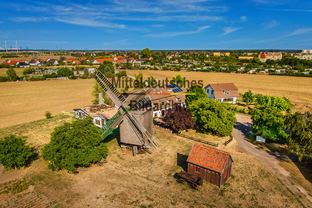Luftbild_Bockwindmühle_Auerbachs_Wolmirstedt-4868 | Das Luftbild zeigt Auerbachs Mühle in Wolmirstedt aus einer Drohnenperspektive. Die historische Mühlenanlage mit ihrem markanten Mühlengebäude und den technischen Einrichtungen vermittelt eindrucksvoll die Bedeutung der Mühlentechnik für die regionale Getreideverarbeitung. Aus der Vogelperspektive werden die baulichen Strukturen und die Lage der Anlage besonders gut sichtbar.Die Mühle wurde im 19. Jahrhundert errichtet und über viele Jahrzehnte kontinuierlich modernisiert. Angetrieben wurde sie zunächst durch Wasserkraft und später mit moderner Antriebstechnik. Walzenstühle, Elevatoren und Förderanlagen ersetzten nach und nach die ursprünglichen Mahlgänge und ermöglichten eine deutlich höhere Mahlleistung sowie einen wirtschaftlicheren Betrieb. Solche Industriemühlen konnten je nach Ausbau täglich mehrere Dutzend Tonnen Getreide verarbeiten und gehörten zu den wichtigsten Versorgungsbetrieben ihrer Region.Die Drohnenaufnahme dokumentiert die historische Industriearchitektur und die technische Entwicklung der Mühlenwirtschaft. Auerbachs Mühle steht beispielhaft für den Wandel von der traditionellen Wassermühle zum modernen Mühlenbetrieb und erinnert an die große wirtschaftliche Bedeutung der Getreideverarbeitung in der Börde und entlang der Ohre. - Realisiert mit Pictrs.com