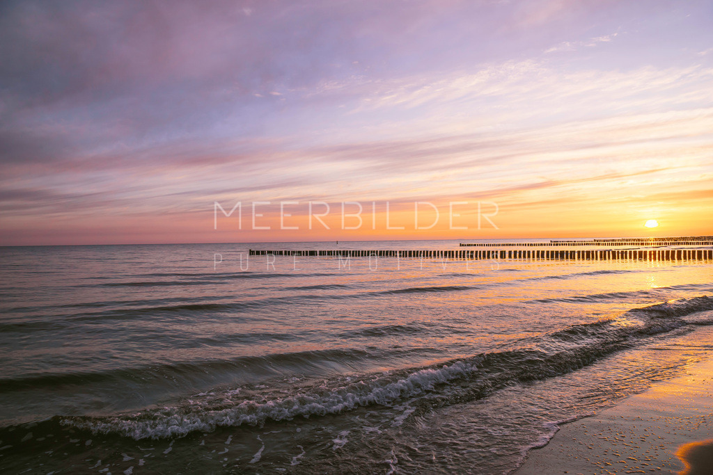 Sonnenaufgang in Zingst // Strandbilder | Ein Sonnenaufgang am frühen Morgen am Strand von Zingst. Leichte Wellen laufen auf den Spülsaum und die Sonne entfaltet immer mehr ihre ganze Kraft. Der Himmel trägt die Farben Lila bis Sonnengelb. Im Hintergrund sind die Buhnenpfähle zu erkennen. 

Wir empfehlen Ihnen dieses Ostseebild auf Alu-Dibond, in Acrylglas oder auf unserem Leinwandklassiker. 
