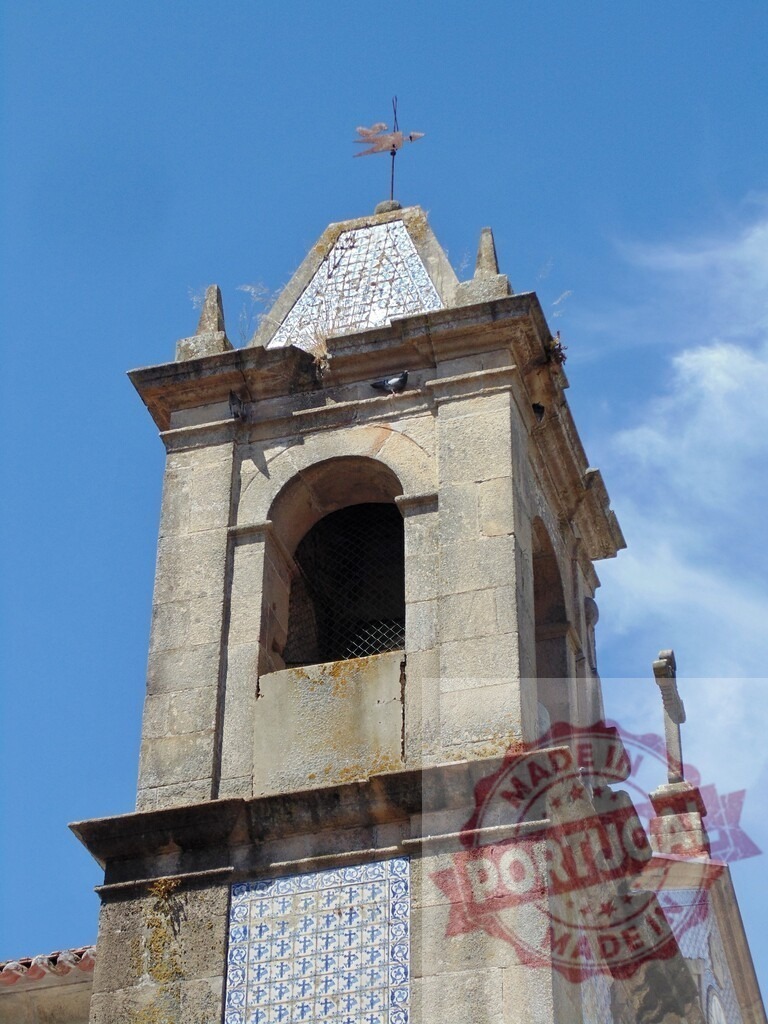 Stone church bell tower with azulejos and weather vane. Aveiro - Portugal | Portuguese church bell tower featuring blue azulejo tiles, a cross, and a weather vane under blue sky - Realized with Pictrs.com
