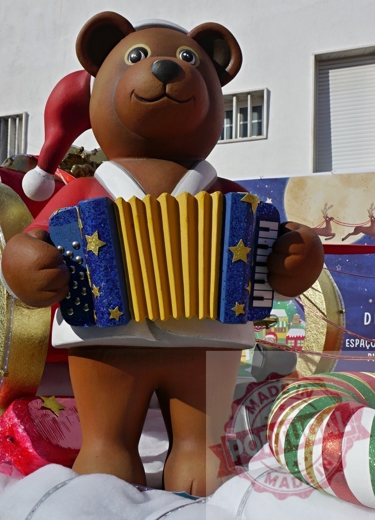 Giant teddy bear playing accordion during Christmas parade | Giant teddy bear dressed as Santa Claus playing a blue and yellow accordion during a Christmas parade - Realisiert mit Pictrs.com