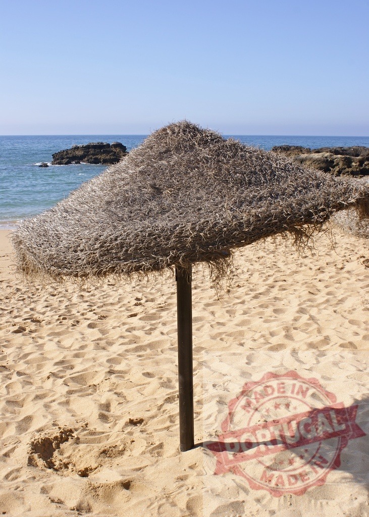 Straw beach umbrella providing shade on sand beach | Straw umbrella offering shade on a sunny sand beach with ocean in background - Realized with Pictrs.com