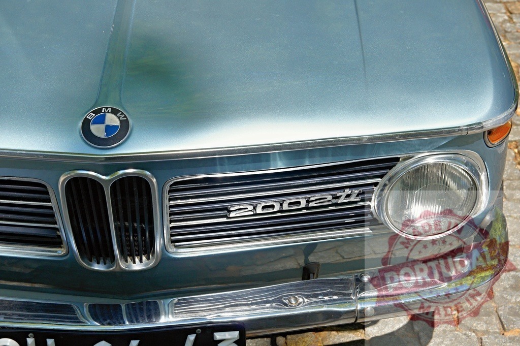 Close-up of BMW 2002ti front grill showing logo and round headlight | Classic BMW 2002ti car parked, showing front grill, logo, and round headlight - Realisiert mit Pictrs.com