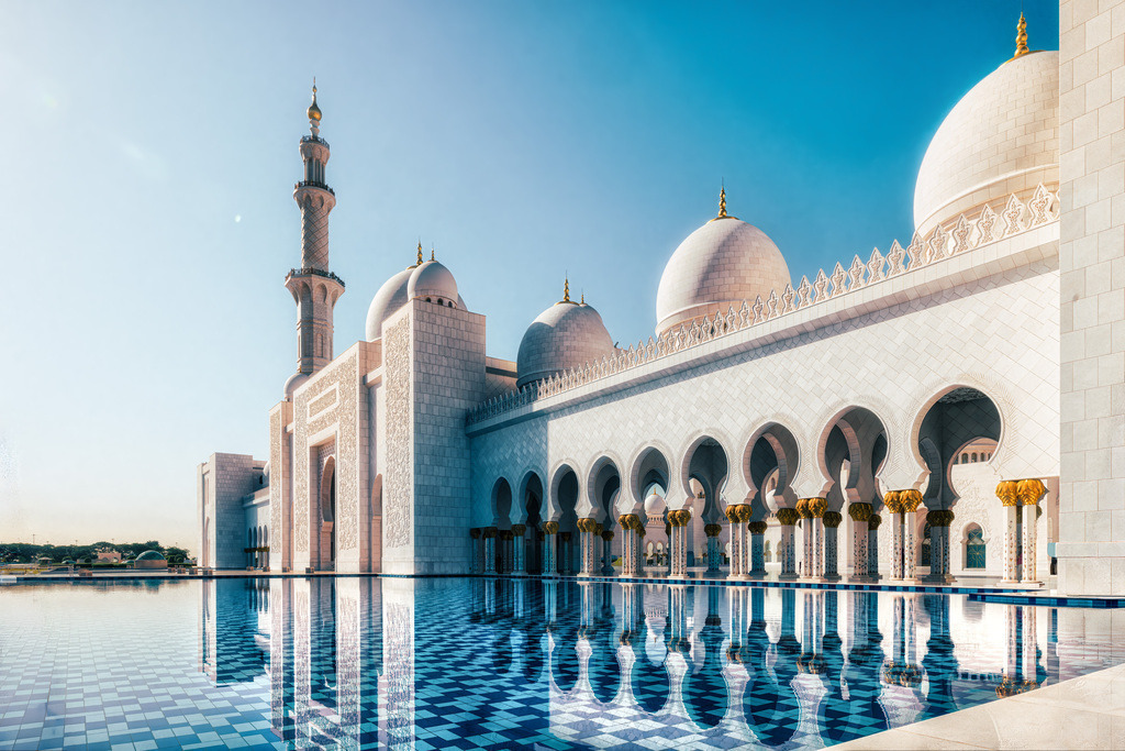 Spiegelung im Wasser der Scheich Zayid Moschee-Abu Dhabi 2 | Die abgebildete Moschee ist die Scheich-Zayid-Moschee in Abu Dhabi, Vereinigte Arabische Emirate. Sie ist die größte Moschee der VAE und eine der größten der Welt. Die Moschee ist für ihre beeindruckende Architektur bekannt, die aus strahlend weißem Marmor, vergoldetem Messing und Swarovski-Kristallen besteht. Sie verfügt über den weltgrößten handgeknüpften Teppich und einen der größten Kronleuchter der Welt. Die Moschee ist eine der wenigen in der Region, die auch Nicht-Muslimen offensteht und den Dialog zwischen verschiedenen Kulturen fördern soll. Der Bau dauerte 12 Jahre und wurde 2007 fertiggestellt; sie bietet Platz für über 40.000 Gläubige. - Realisiert mit Pictrs.com