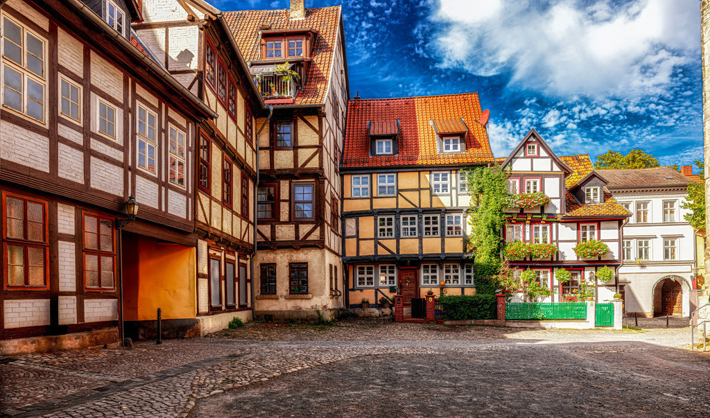 Aufnahme eines bunten Fachwerk-Ensemble in Quedlinburg,Harz | Das Bild zeigt die historische Altstadt von Quedlinburg, ein berühmtes Fachwerk-Ensemble im Harz, Sachsen-Anhalt. Quedlinburg besitzt über 1.300 Fachwerkhäuser aus sechs Jahrhunderten und zählt zum UNESCO-Weltkulturerbe. Die Stadt ist bekannt für ihre architektonische Vielfalt, die Stile von der Renaissance bis zum Klassizismus umfasst. Sie gilt als eine der bedeutendsten Fachwerkstädte Deutschlands. Die malerischen Gassen und gut erhaltenen Gebäude ziehen zahlreiche Besucher an.  - Realisiert mit Pictrs.com