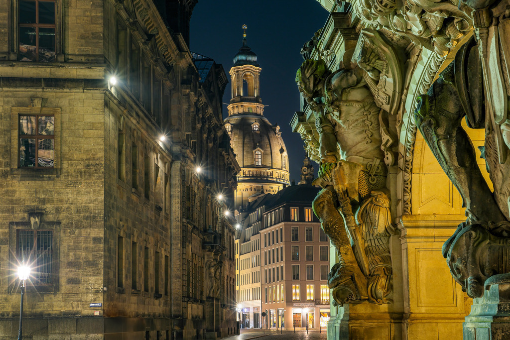 Blick zur Frauenkirche - Dresdens stille Nacht | Dieses Wandbild fängt einen der magischsten Blicke auf die Dresdner Frauenkirche ein. Zwischen barocken Fassaden und kunstvollen Skulpturen eröffnet sich ein klarer Blick auf die angestrahlte Kuppel, eingerahmt von historischer Architektur und nächtlicher Stille. Die warme Beleuchtung und die Tiefe der Komposition verleihen dem Motiv eine geheimnisvolle, fast filmische Atmosphäre. Ideal für alle, die Details, Geschichte und eine besondere Perspektive auf die Altstadt zu schätzen wissen.