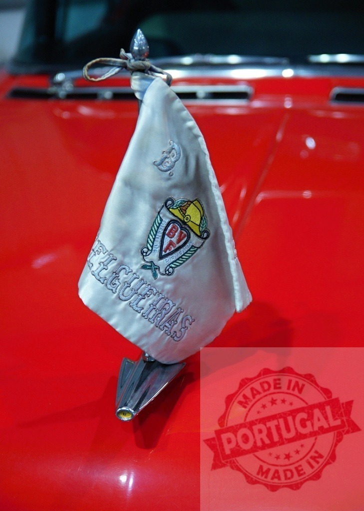 White pennant waving on a red car hood | Close-up of a white pennant with an embroidered logo, attached to the hood of a gleaming red car - Realisiert mit Pictrs.com