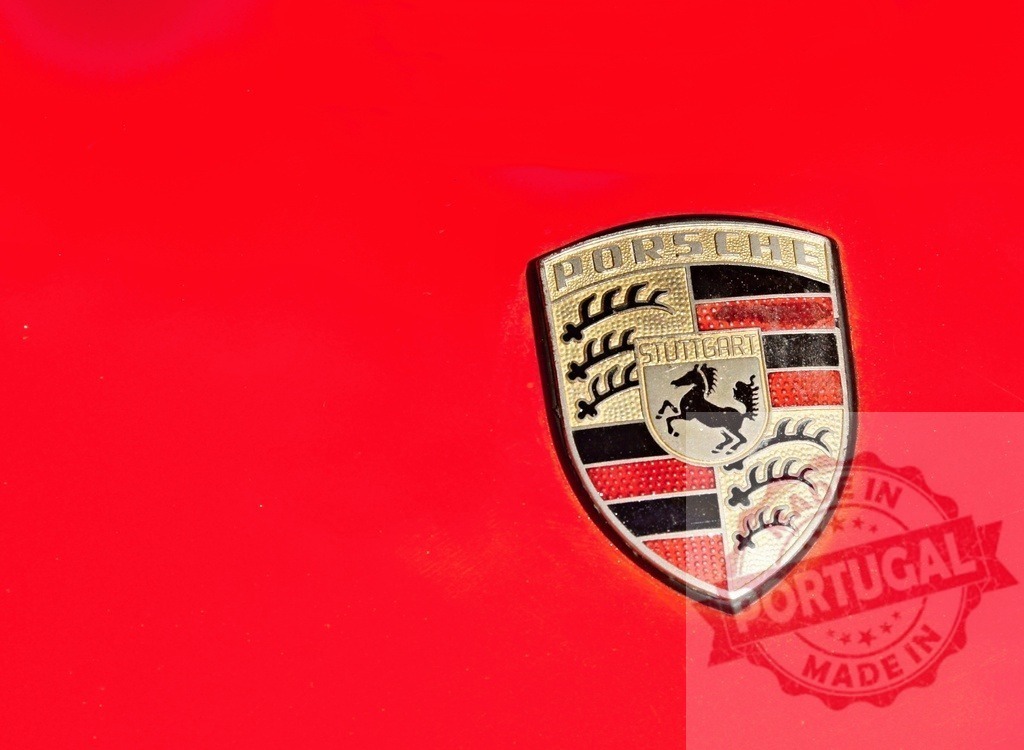 Porsche logo shining on a red car body | Close-up of the Porsche logo on a red car, representing luxury, performance, and automotive excellence - Realisiert mit Pictrs.com
