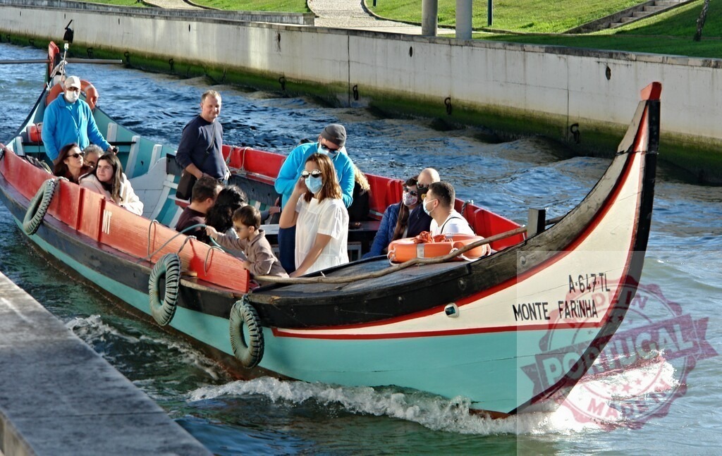 Moliceiro boat carrying tourists on Aveiro canal navigating | Traditional Moliceiro boat carrying tourists wearing face masks navigating a canal in Aveiro, Portugal - Realized with Pictrs.com