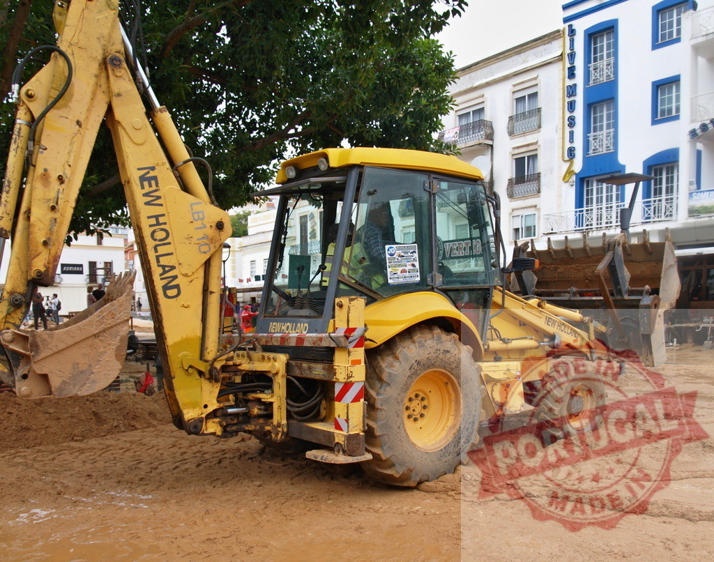 New Holland backhoe loader working urban mud street | Albufeira Flood - discruction by weather problems Yellow New Holland backhoe loader working on a muddy urban construction site - Realized with Pictrs.com