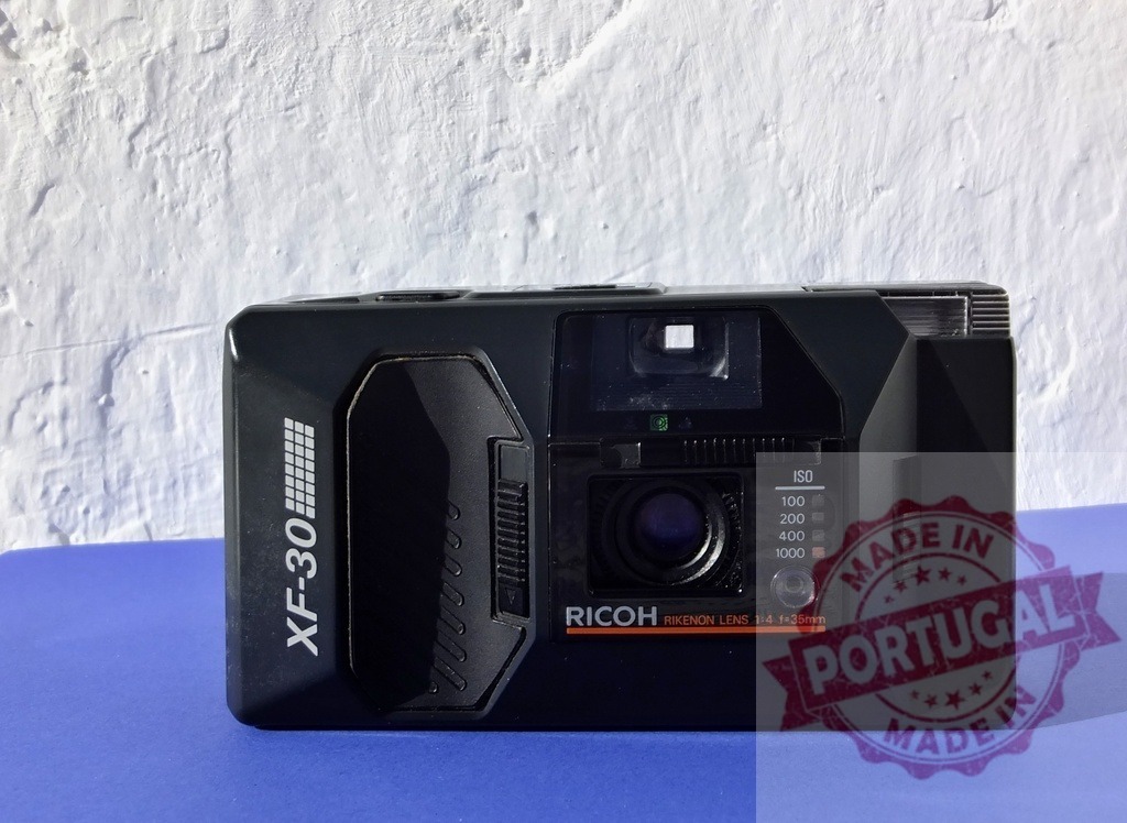 Ricoh XF-30 film camera vintage analog technology | Ricoh XF-30 compact film camera resting on a blue surface - Realized with Pictrs.com