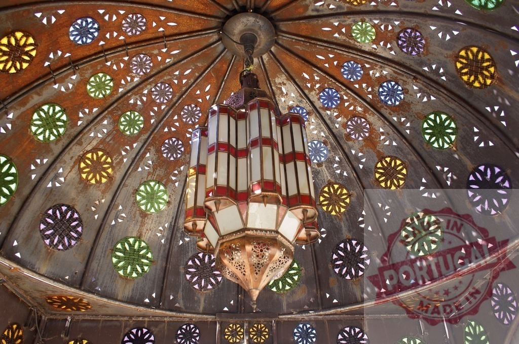 Moroccan lantern illuminating intricate stained glass ceiling dome | Moroccan lantern creating a colorful light display on a detailed metal and stained glass ceiling - Realisiert mit Pictrs.com