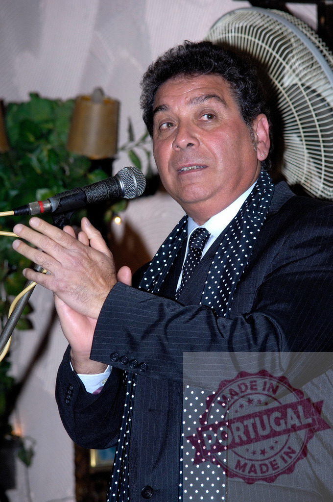 Enrico Macias performing live concert, clapping hands by microphone | Enrico Macias clapping during a live performance by a microphone, wearing a pinstripe suit and polka dot tie - Realized with Pictrs.com