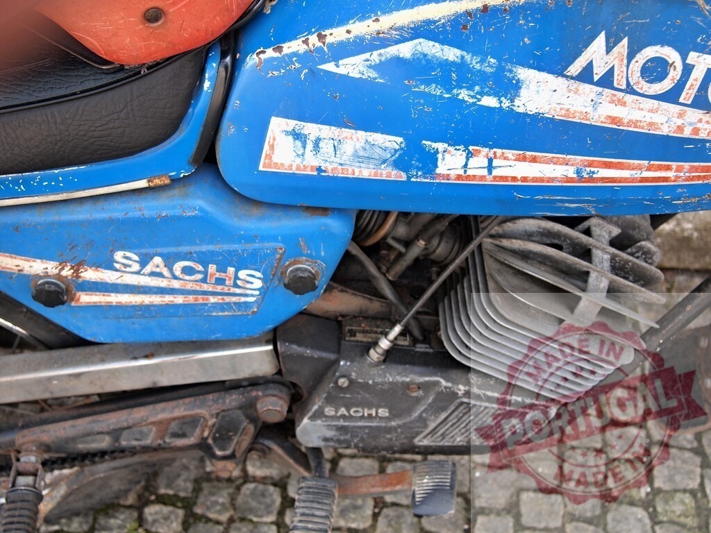 Close-up of rusty Sachs engine of a vintage blue motorcycle | Old and rusty Sachs engine of a vintage blue motorcycle parked on a cobblestone street - Realized with Pictrs.com