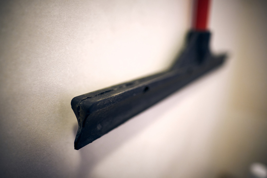 Fliesenabzieher mit rotem Stil hängt an der Wand | Austria - January 18, 2021: Fliesenabzieher mit rotem Stil hängt an der Wand. - Realisiert mit Pictrs.com