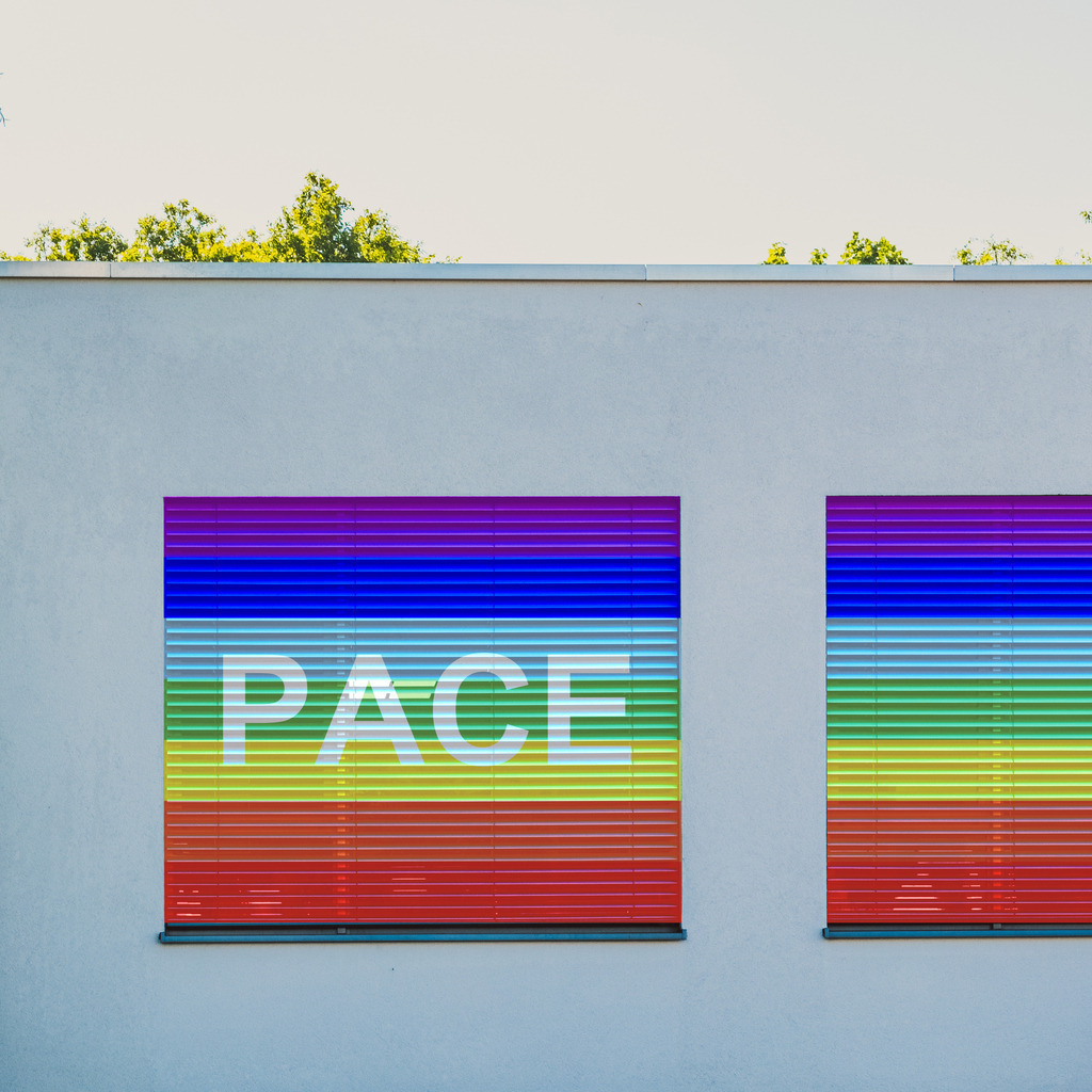 Pace Flagge auf Fenster Rolladen | Regenbogenfahne der Friedensbewegung („Pace-Flagge“) mit weißer Friedenstaube. Pace (lateinisch.) = Frieden.