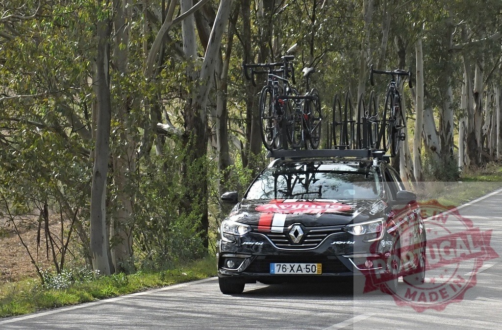 Renault support vehicle carrying bicycles on a rural road | Renault support car with bicycles on roof rack driving through a tree-lined road - Realized with Pictrs.com