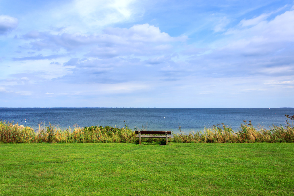Wandbild: Bank am Strand in Norgaardholz | Dieses Wandbild im Querformat zeigt eine schöne Bank am Strand in Norgaardholz. Der Himmel ist überwiegend bewölkt.  - Realisiert mit Pictrs.com