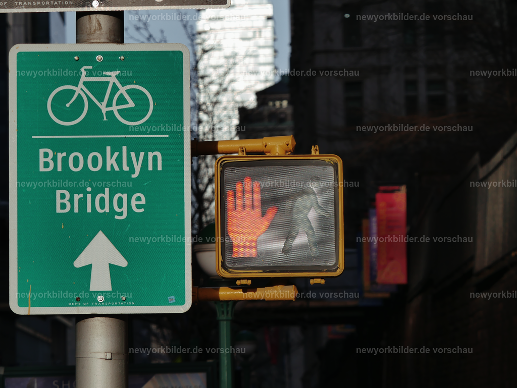 Brooklyn Bridge Radweg & Lichtsignal – Ikonische Symbole von New York City | Dieses Bild fängt die Essenz von New York City in kleinen Details ein: ein Lichtsignal für Fußgänger und das Schild für den Radweg zur Brooklyn Bridge. Zwei unscheinbare Elemente, die doch so viel über die Stadt erzählen. Hier beginnt für viele ein Weg voller Geschichten – die Brooklyn Bridge, ein weltberühmtes Wahrzeichen, das Menschen verbindet und täglich von Radfahrern, Spaziergängern und Touristen überquert wird. Das Lichtsignal steht für Bewegung, für den Rhythmus der Metropole, die niemals stillsteht.