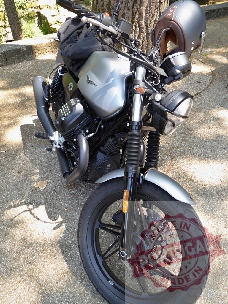 Moto Guzzi V7 Stone motorcycle parked in the shade | Moto Guzzi V7 Stone motorcycle with a brown helmet hanging from the handlebar parked in the shade of a tree - Realisiert mit Pictrs.com