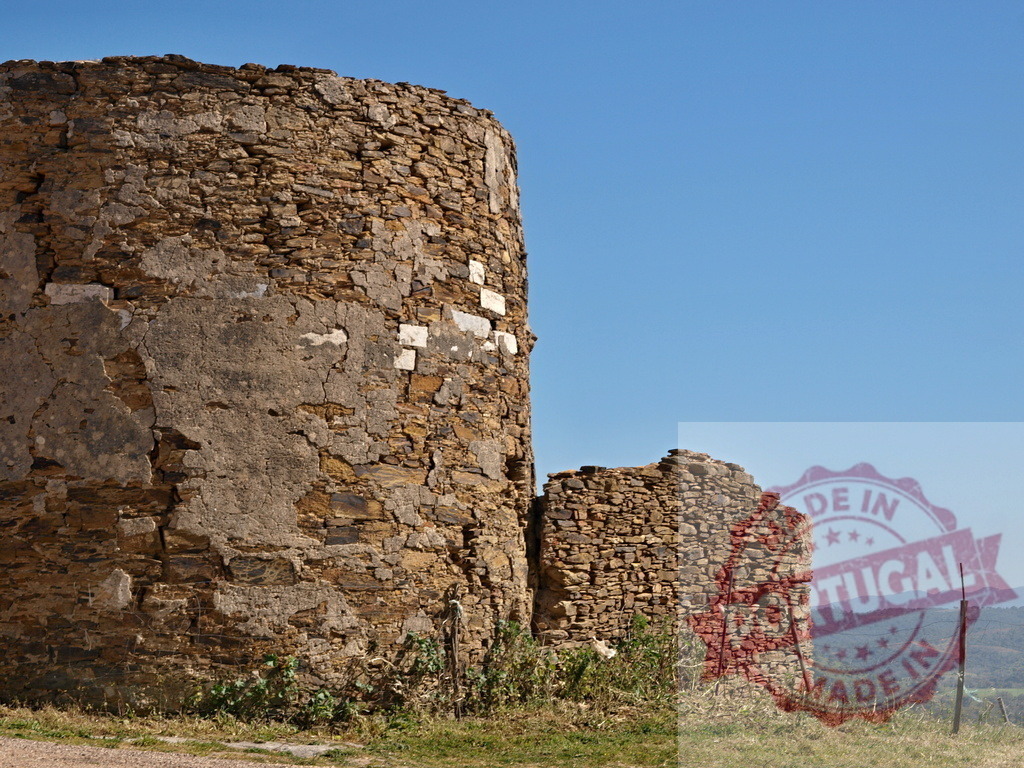 Ancient stone tower ruins standing under blue sky | Old stone tower and wall remnants showing historical decay on a clear day - Realized with Pictrs.com
