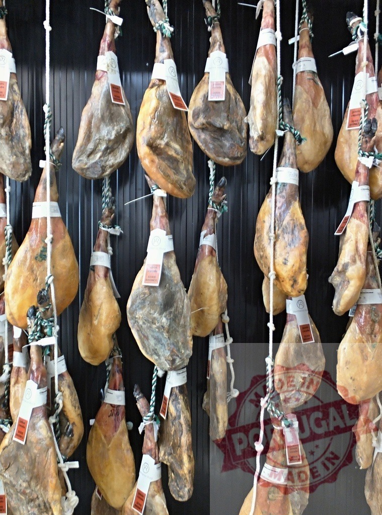 Jamón Serrano hanging in a Spanish delicatessen | Cured ham legs hanging in rows in a traditional Spanish market - Realized with Pictrs.com