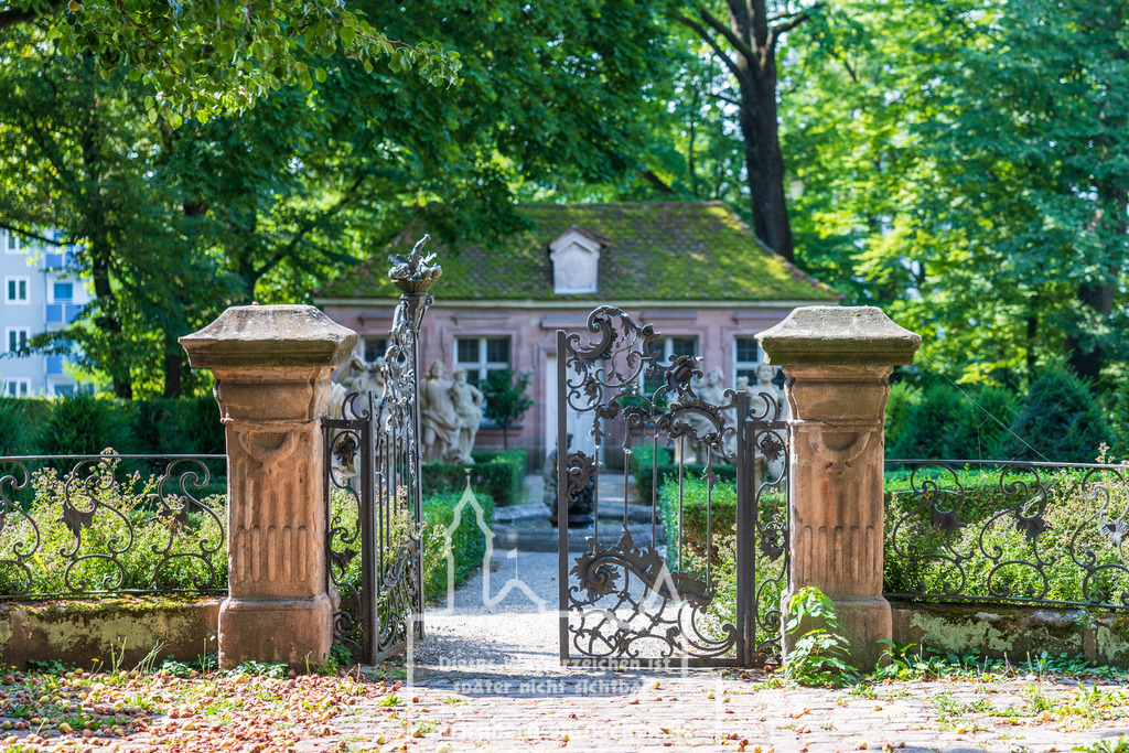Monatsbild des Kalender 2026 für den Monat August | Eingang zu den Hesperidengärten in Nürnberg bei der Johannisstraße 13. Das schmiedeeiserne Tor mit kunstvollen Ornamenten öffnet den Blick auf die barocke Gartenanlage mit symmetrischen Hecken, Sandsteinfiguren und historischem Gartenhaus im Hintergrund. Alte Bäume spenden im Sommer reichlich Schatten und schaffen eine angenehme Atmosphäre. Die Hesperidengärten zählen zu den bedeutenden Gartenanlagen der Stadt und sind ein beliebtes Ziel für Besucher. - Realisiert mit Pictrs.com