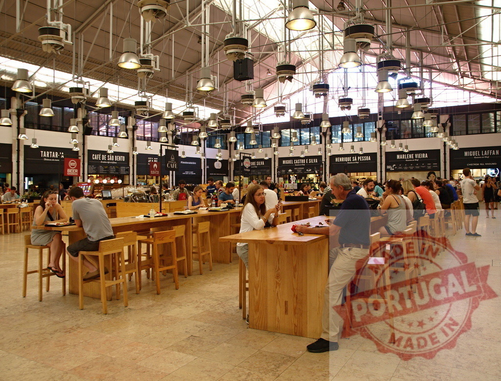 Time Out Market Lisbon food court communal dining experience. Lisbon - Portugal | People enjoying food and drinks at communal tables inside a large market hall - Realized with Pictrs.com