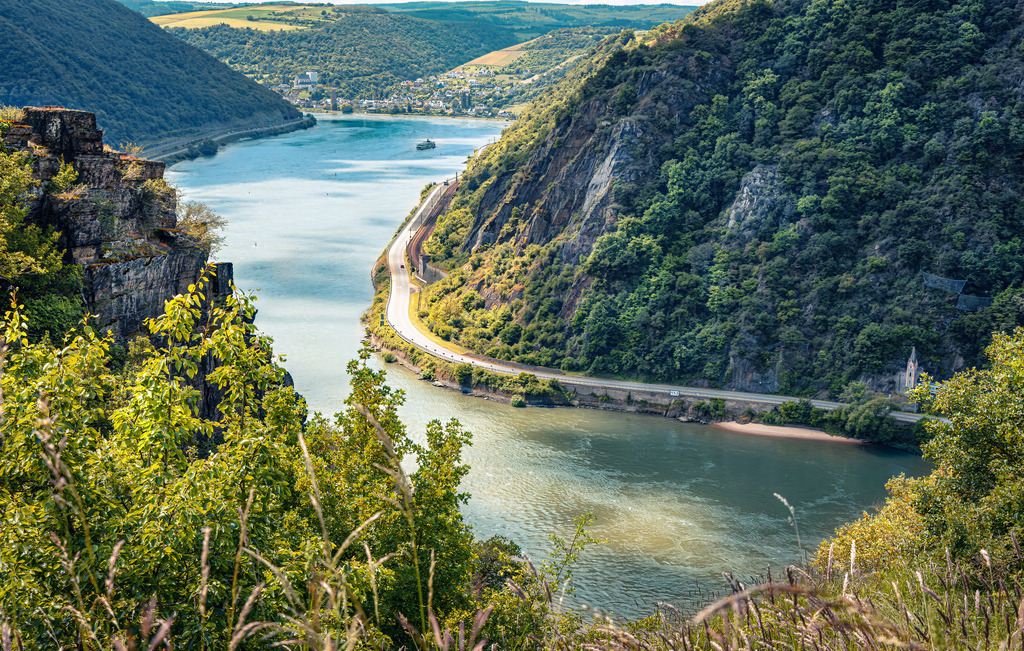 Ausblick von Spitznack auf die malerische Rheinschleife im Mittelrheintal,Loreley | Das Bild zeigt den Ausblick vom Aussichtspunkt Spitznack (einem markanten Felsvorsprung auf dem Rheinsteig nahe St. Goarshausen) hinab auf eine malerische Rheinschleife im UNESCO-Welterbe Oberes Mittelrheintal in Rheinland-Pfalz.Der Spitznack erhebt sich steil über dem rechten Rheinufer südlich der berühmten Loreley.Wandern: Der Ort liegt direkt auf der anspruchsvollen und aussichtsreichen Route des Rheinsteig-Wanderwegs.Landschaft: Von hier aus blickt man auf den tief eingeschnittenen Strom des Rheins, steile Schieferfelsen und bewaldete Hänge - Realisiert mit Pictrs.com
