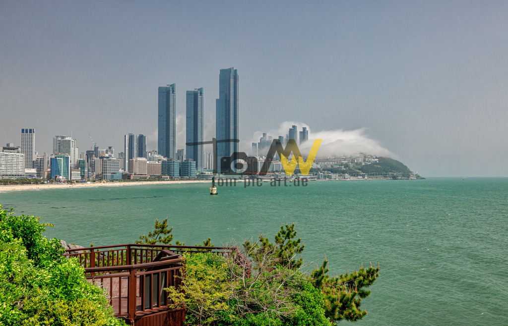 Blick auf den Heaundae Strand in Busan mit Skyline,Südkorea | Das Bild zeigt den Haeundae Beach und den angrenzenden Dongbaek Park in Busan, Südkorea. Die Aufnahme wurde wahrscheinlich vom Dongbaek Park aus gemacht und bietet einen Panoramablick auf die Küste und die Skyline der Stadt. Hier sind einige wichtige Details:Standort: Der Dongbaek Park liegt auf der ehemaligen Insel Dongbaekseom am südlichen Ende des Haeundae Beach und ist heute durch Sedimentation mit dem Festland verbunden. Aussicht: Der Park bietet malerische Ausblicke auf das Meer, den Strand und die Hochhäuser von Haeundae.  - Realisiert mit Pictrs.com