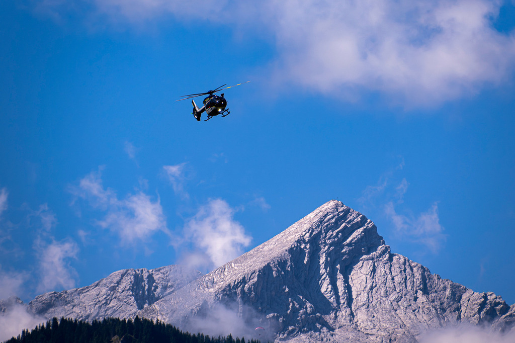 Wachposten über den Gipfeln: „Edelweiß“ im Alpineinsatz | Erhaben zieht ein H145 der bayerischen Polizeihubschrauberstaffel „Edelweiß“ seine Bahnen vor der imposanten Kulisse der Alpspitze bei Garmisch-Partenkirchen. Vor strahlend blauem Himmel und den gewaltigen Felsmassiven der Alpen wirkt die hochmoderne Maschine wie ein wachsamer Schutzengel. Wo majestätische Natur und alpine Herausforderungen aufeinandertreffen, sorgt die Besatzung für Sicherheit aus der Luft. Ein eindrucksvolles Zusammenspiel aus der Freiheit der Berge und fliegerischer Präzision. - Realisiert mit Pictrs.com
