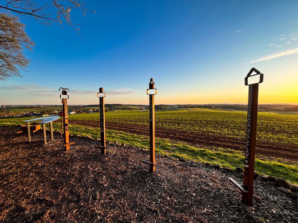 Eisenstelen - Wenings | Oberhalb von Wenings auf dem Weg nach Gedern liegt ein liebevoll gestalteter Aussichtspunkt. Mit einem Ensemble der Materialen Holz, Stein und Metall wird die Vielfältigkeit der Region in Szene gesetzt. Bereits die kleinsten Einwohner zieht es während eines Naturtages des Kindergartens zur Hügelkuppel. Für Groß und Klein eröffnet sich eine Welt des Ausprobierens und Erlebens. So wird Natur greifbar. - Realisiert mit Pictrs.com