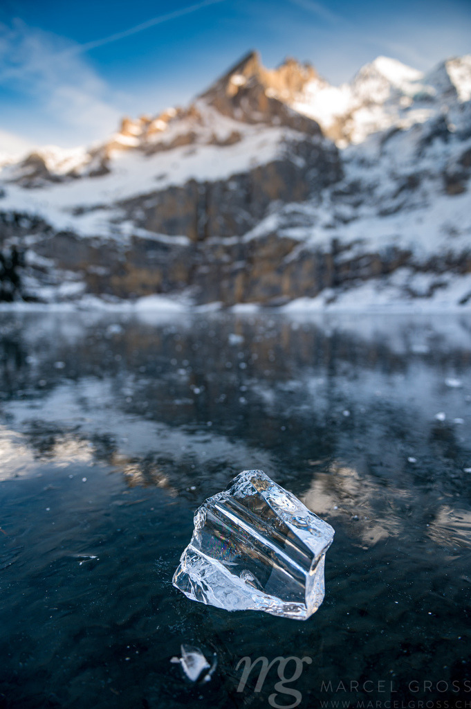 beautiful clear chunk of ice on frozen lake Oeschinensee with reflection and Blümlisalp Mountains in Berner Oberland | Die ideale Geschenkidee für Naturliebhaber. Naturbilder von Marcel Gross Photography für ihr Zuhause in den verschiedensten Formaten und Materialien. - Realisiert mit Pictrs.com