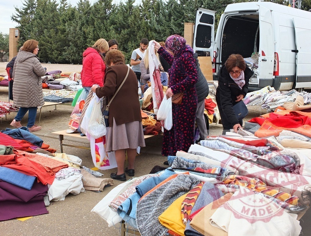 People shopping for textiles at outdoor street market | Shoppers browsing and selecting colorful fabrics and clothing at an outdoor market stall - Realisiert mit Pictrs.com