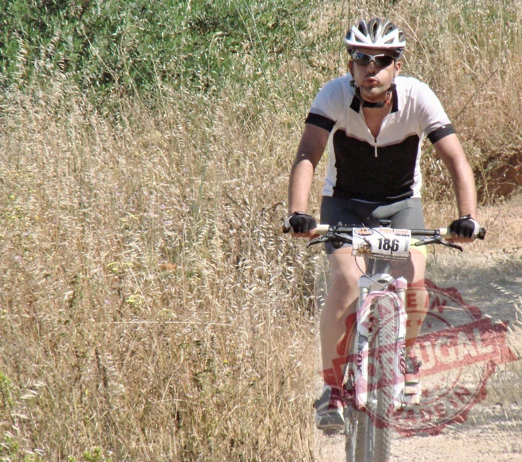 Mountain biker enjoying a ride on a sunny day | Cyclist wearing helmet riding mountain bike on a trail near tall grass - Realisiert mit Pictrs.com