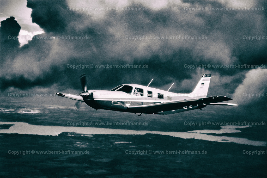 PLBDD_air2air_PiperSara_04b_90x60 | Luftbild, einmotoriges Geschäftsflugzeug Typ " PIPER Saratoga II TC " zwischen den Wolken. Sonnenstrahlen erhellen die Szenerie. Flug nördlich der Schlei mit der Stadt Schleswig. ___ Das Foto ist eine Reproduktion von einem Farbdia. Bildanmutung = schwarz-weiß Charakter mit schwacher Farbtonung. - Realisiert mit Pictrs.com