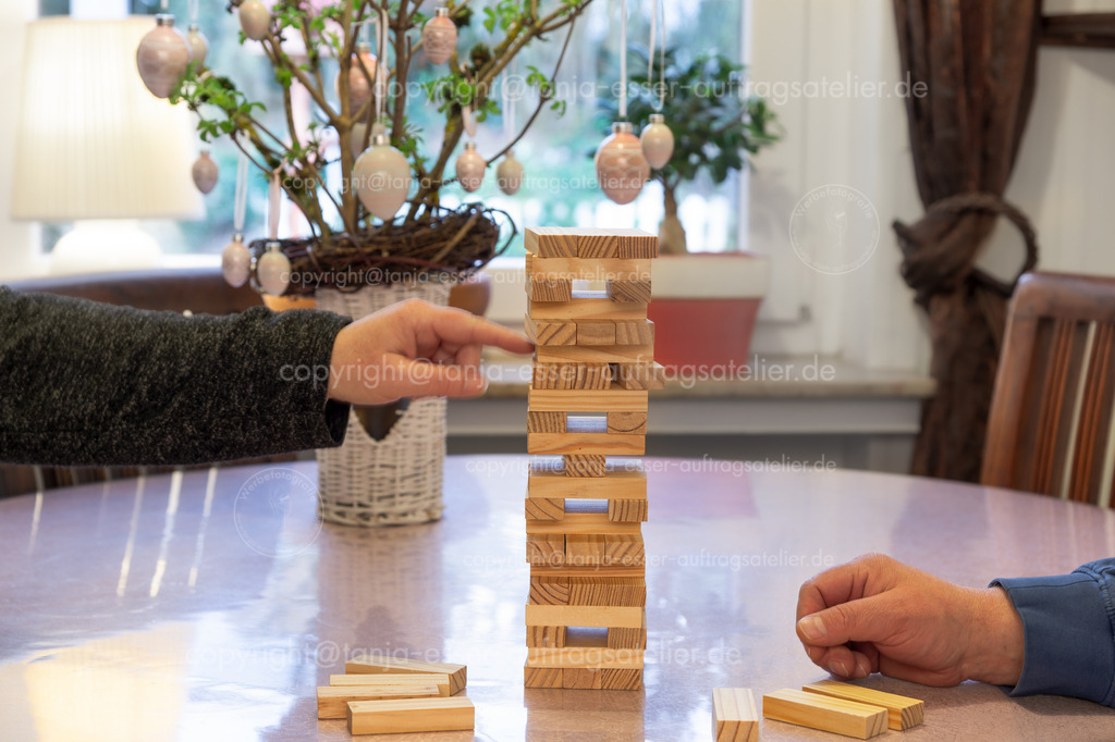 OsternGesellschspiel 2 D | In der Osterzeit spielt die Familie zusammen Gesellschaftsspiele. Frau und Mann bauen einen wackeligen Turm aus Holzblöcken. Im Hintergrund steht der Osterstrauß mit Ostereiern. Bewegungsunschärfe. 