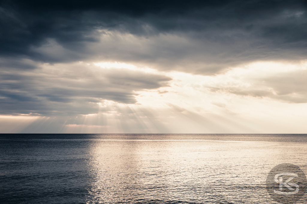 Dramatische Meereslandschaft bei Sonnenaufgang, bedeckter Himmel | Tauchen Sie ein in die dramatische und fesselnde Schönheit dieser Meereslandschaft. Der Kontrast zwischen den dunklen Gewitterwolken und dem hellen Sonnenlicht, das auf die Wasseroberfläche fällt, schafft eine intensive Atmosphäre und ein faszinierendes Lichtspiel am Horizont. - Realisiert mit Pictrs.com