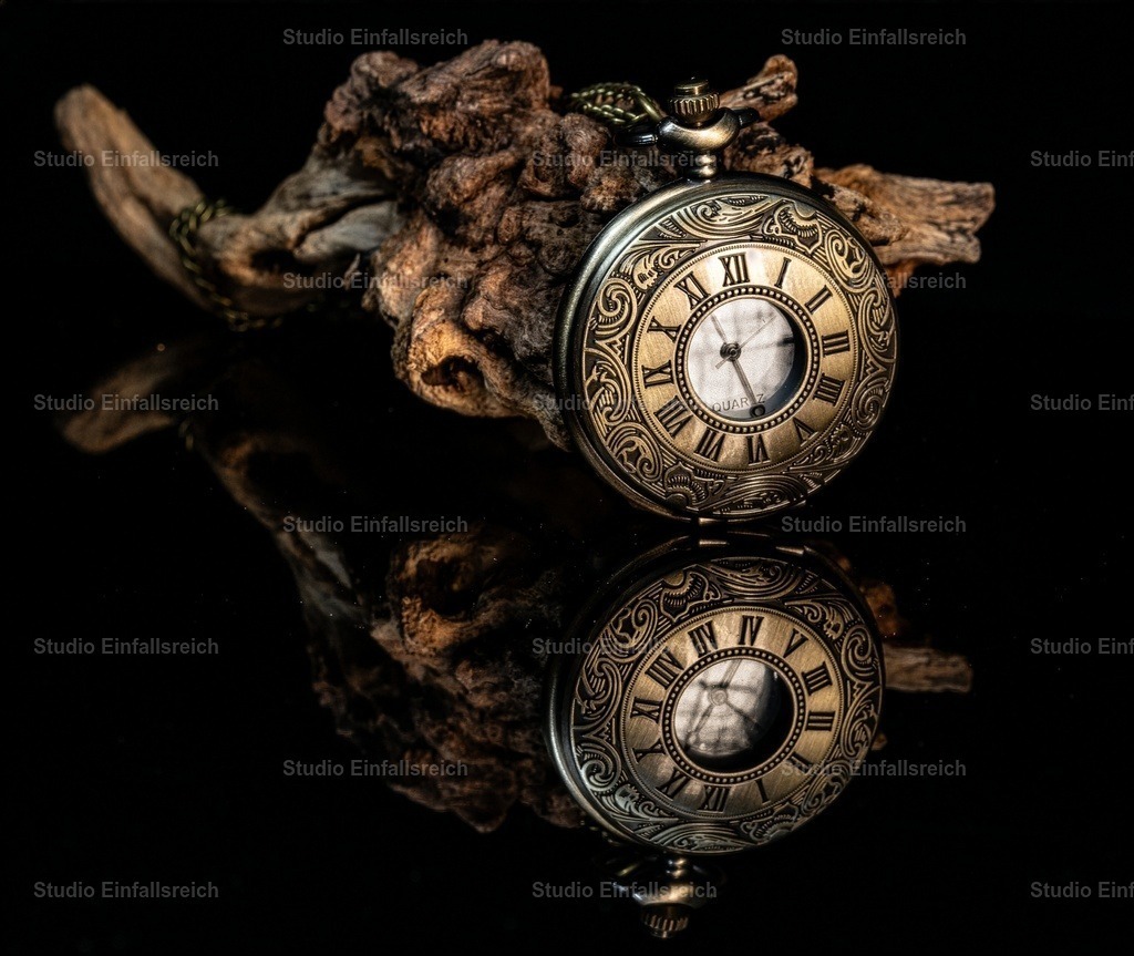 Zeitlos – Taschenuhr auf Wurzelholz | Eine kunstvoll gravierte Taschenuhr ruht auf altem Wurzelholz und spiegelt sich auf schwarzer Fläche. Warmes Messing, römische Ziffern und feine Ornamente erzählen von vergangener Zeit. Ein edles Motiv mit Charakter. Als Fine-Art-Print und Wandbild in verschiedenen Größen erhältlich. - Realisiert mit Pictrs.com