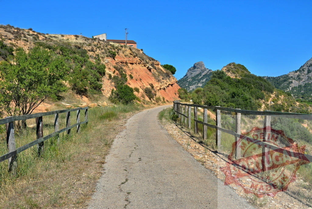 Unpaved rural road winding through mountainous landscape | Unpaved rural road extending through a green and rocky mountainous landscape under a clear blue sky - Realisiert mit Pictrs.com