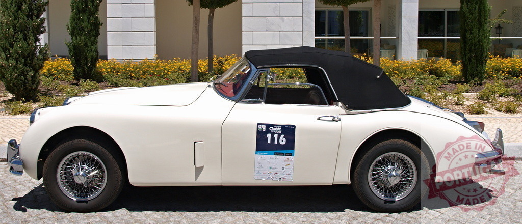 White Jaguar XK150 Roadster Participating in Classic Car Rally | Classic white Jaguar XK150 Roadster with a black convertible top parked near a building, possibly during a classic car rally or exhibition - Realisiert mit Pictrs.com
