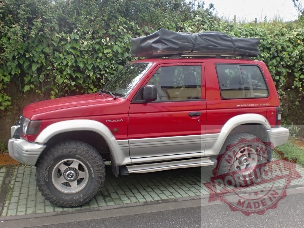 Red Mitsubishi Pajero SUV parked outdoors with a roof rack and tent | Red Mitsubishi Pajero SUV with rooftop tent ready for off-road adventure - Realized with Pictrs.com